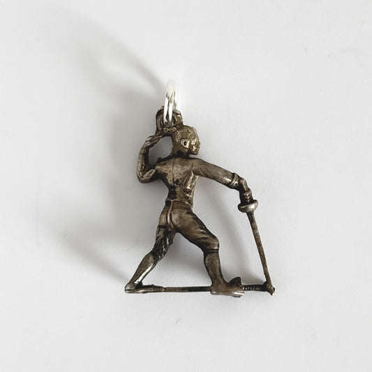 Silver pendant of a person fencing holding a sword on a white background