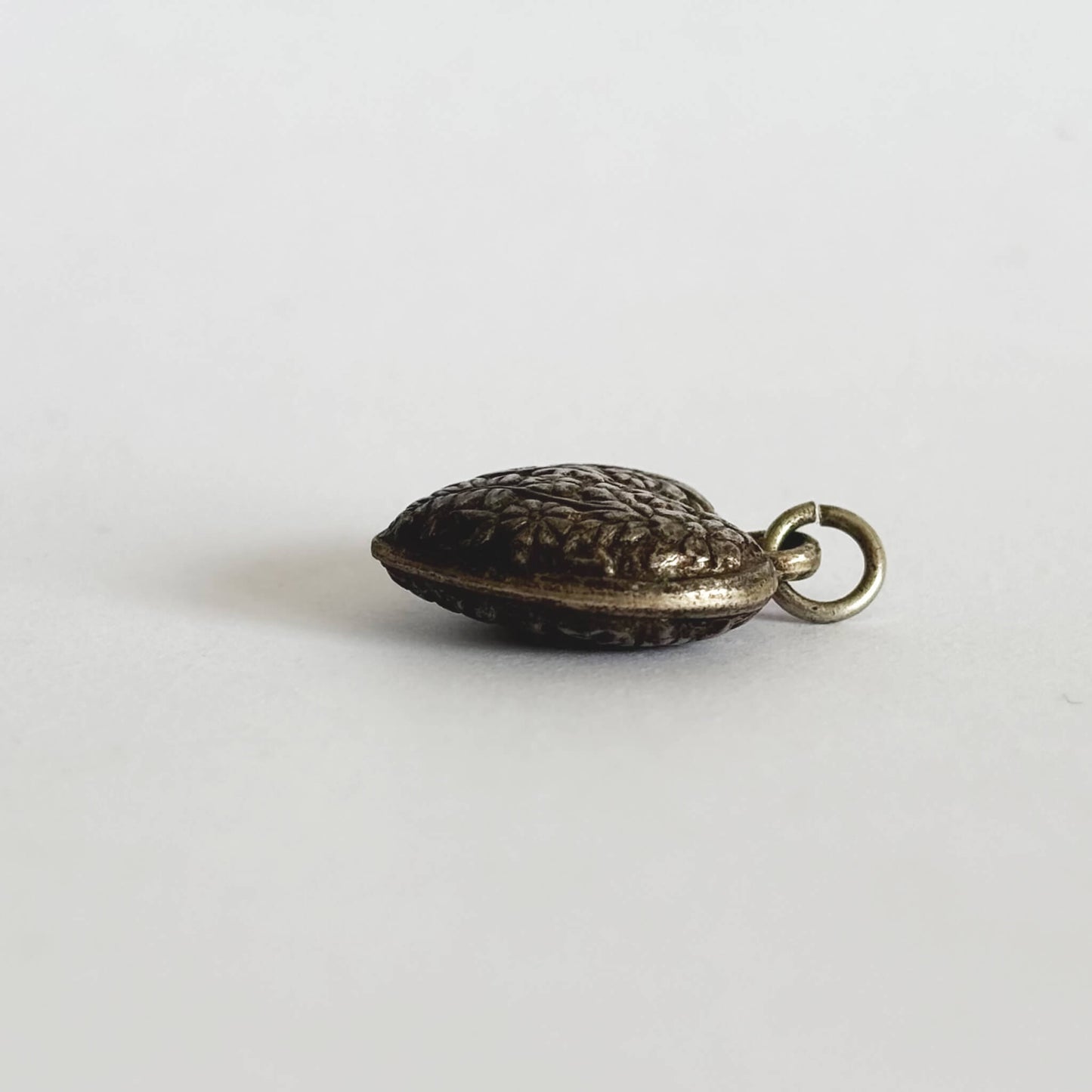 dark silver puffed heart charm with a textured surface seen from side on a white background