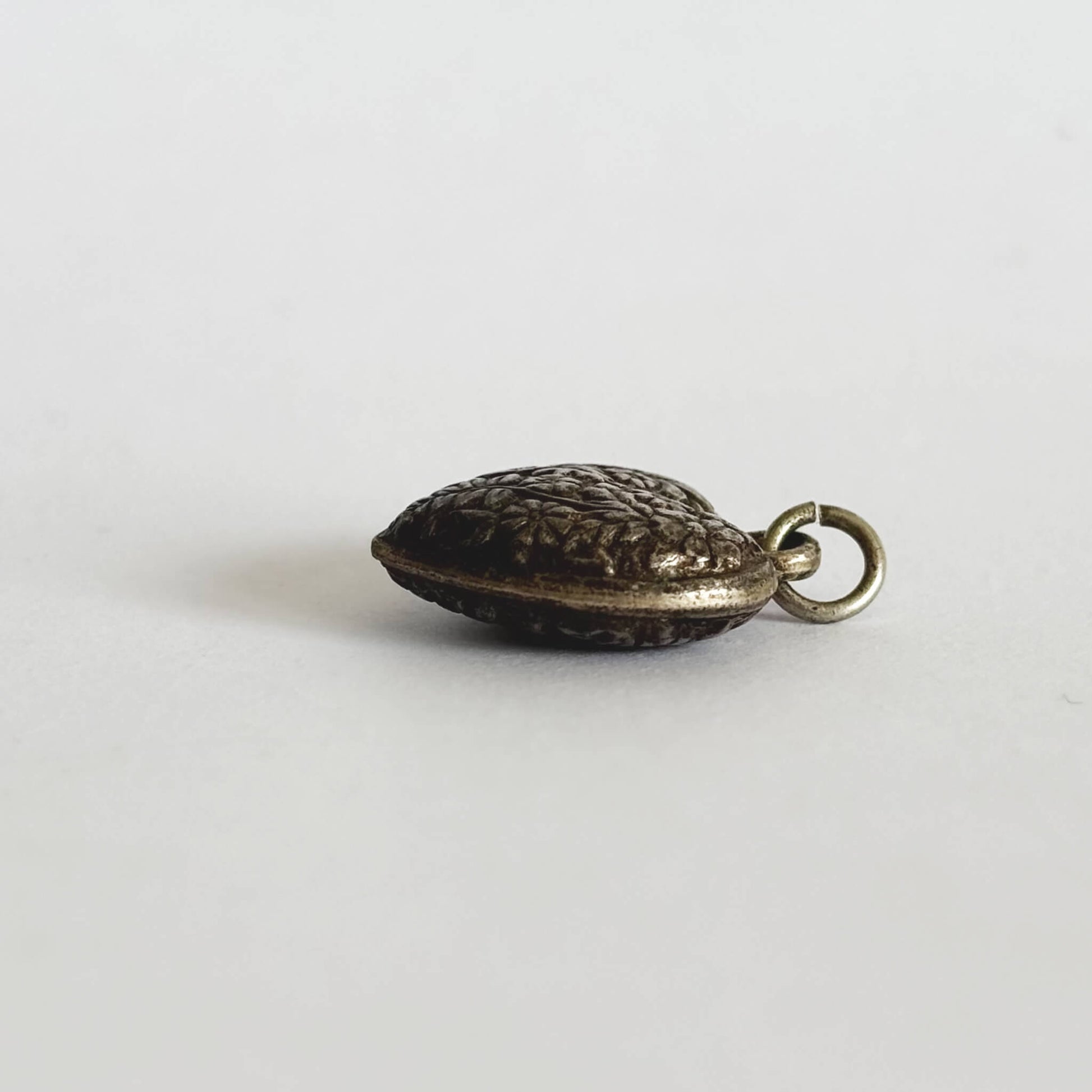 dark silver puffed heart charm with a textured surface seen from side on a white background