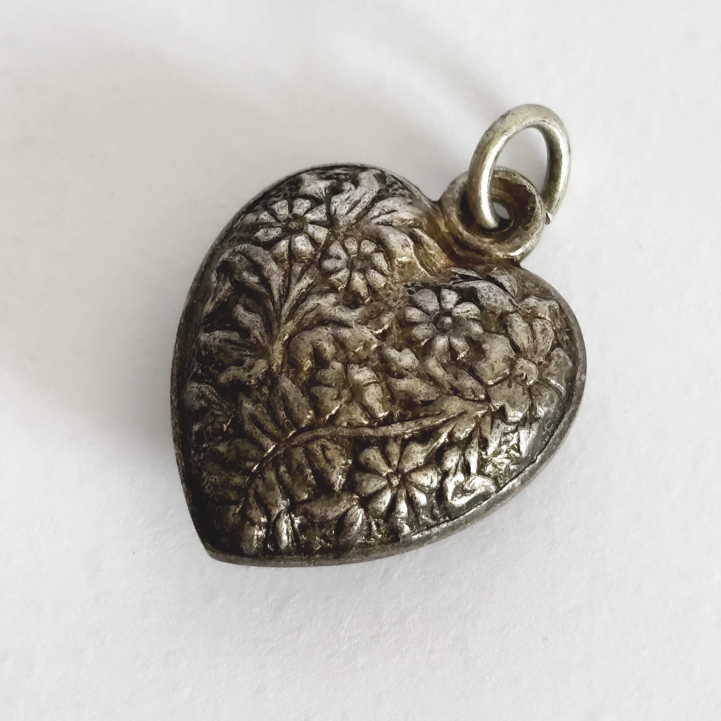 Silver heart-shaped pendant with floral engraving on a white background