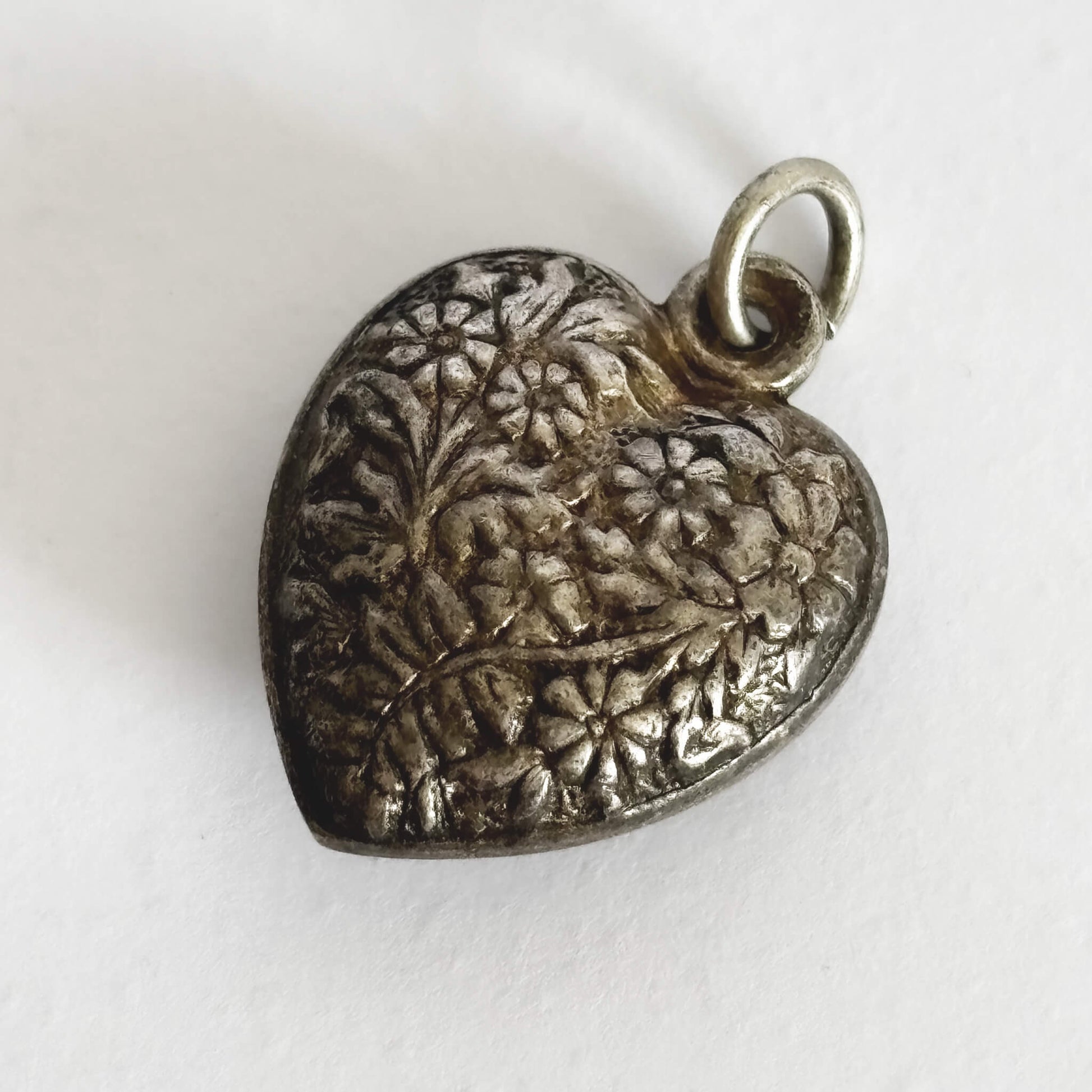 Silver heart-shaped pendant with floral engraving on a white background