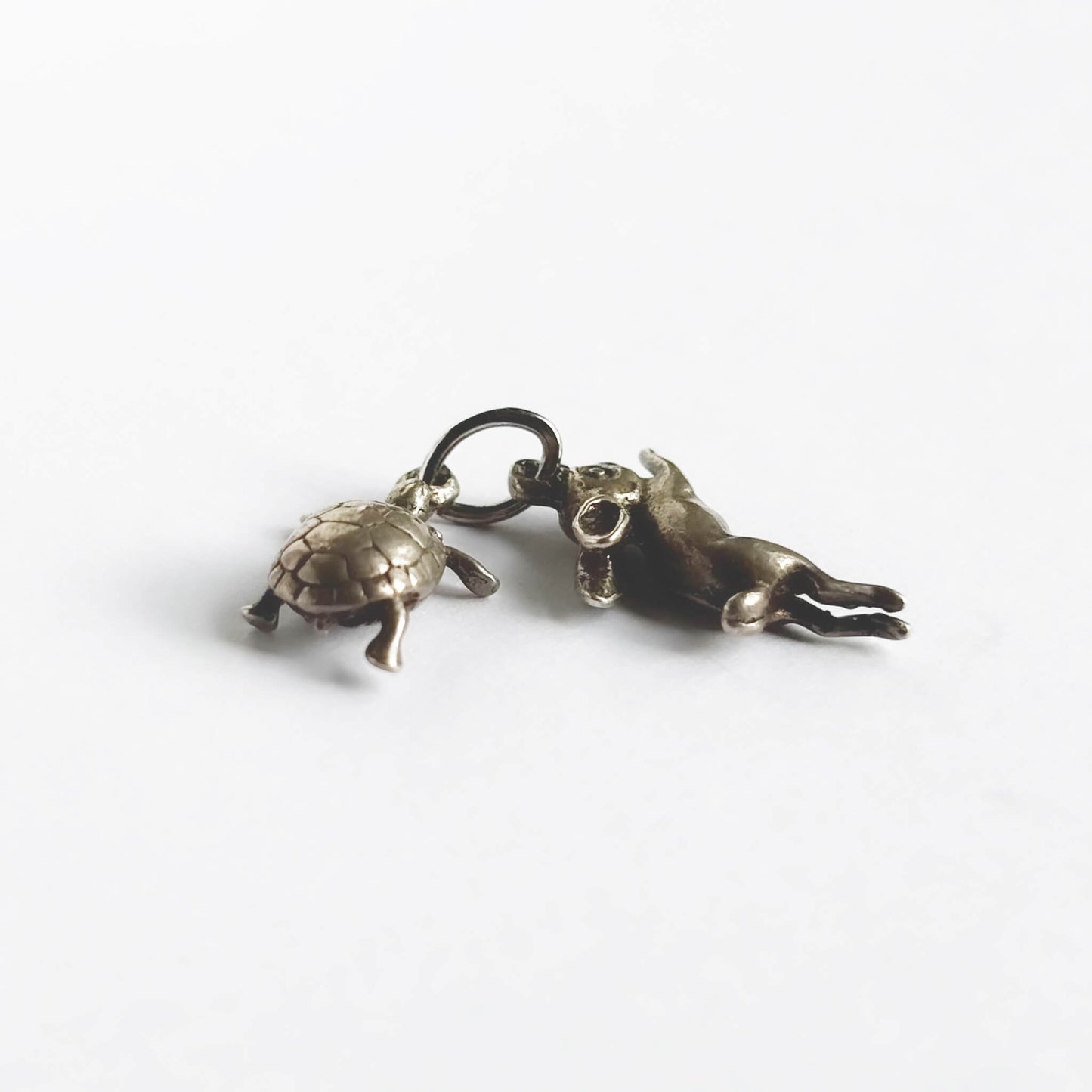 A vintage silver hare and tortoise charm on a white background.