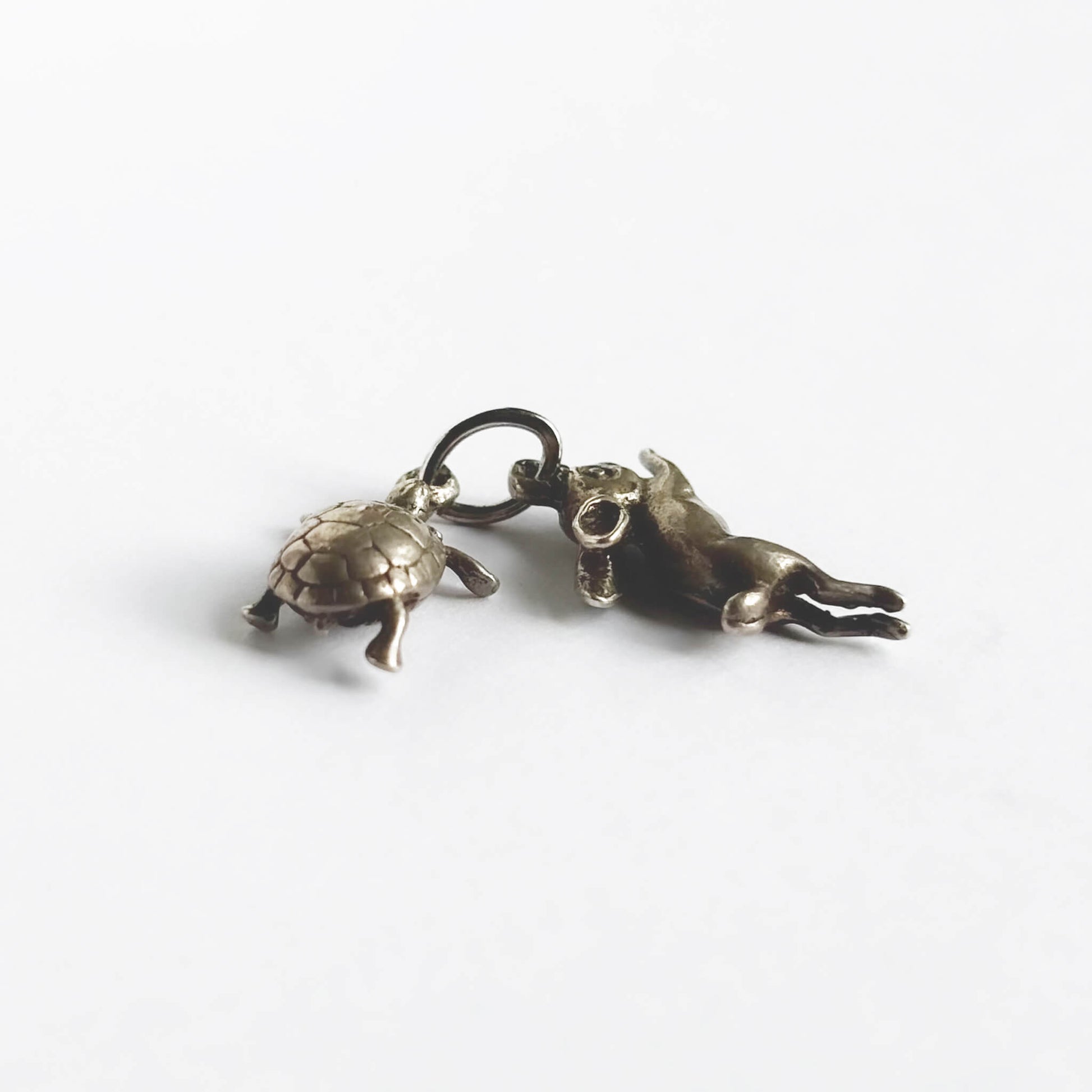 A vintage silver hare and tortoise charm on a white background.