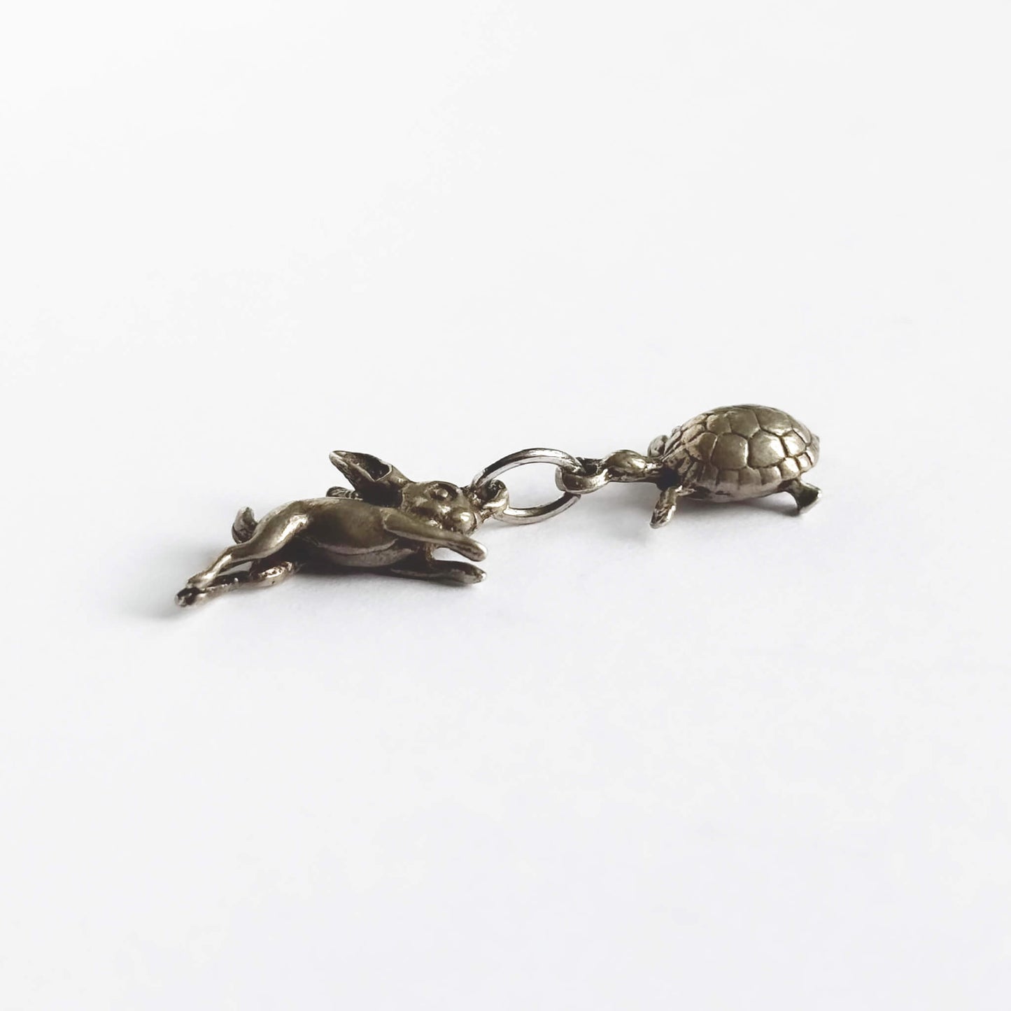 A vintage silver hare and tortoise charm on a white background.