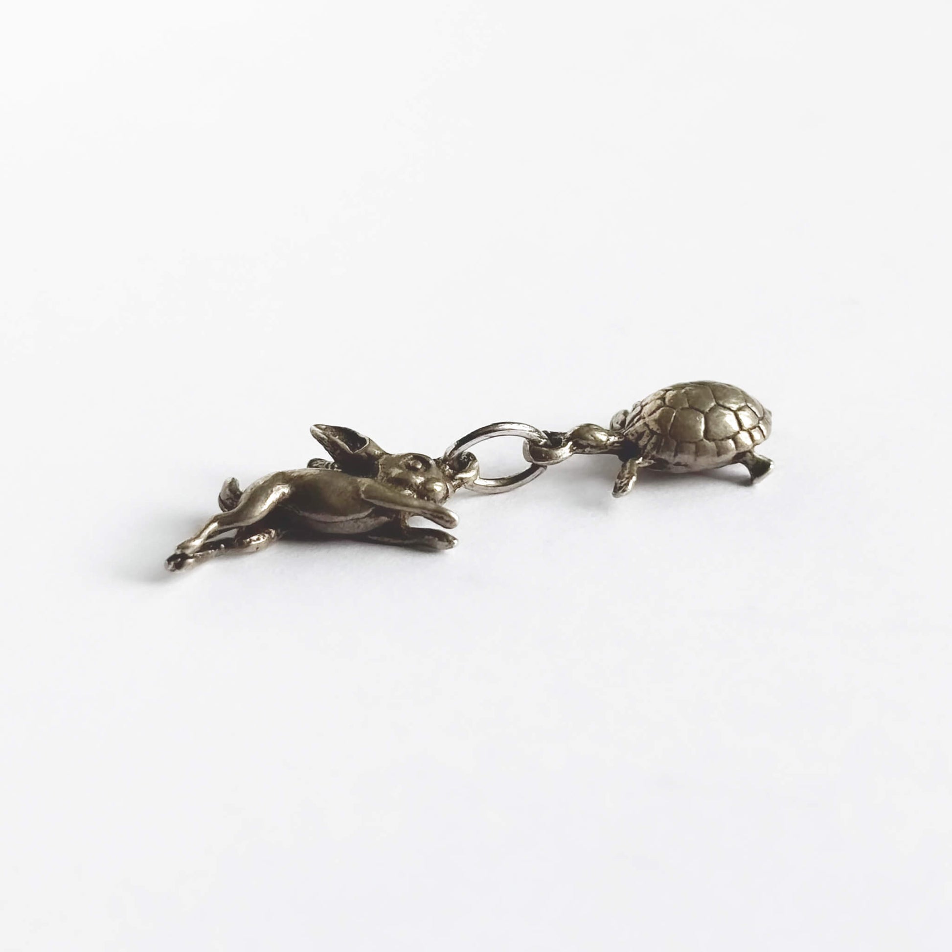 A vintage silver hare and tortoise charm on a white background.