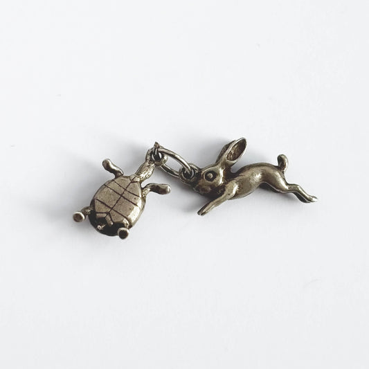 A vintage silver hare and tortoise charm on a white background.