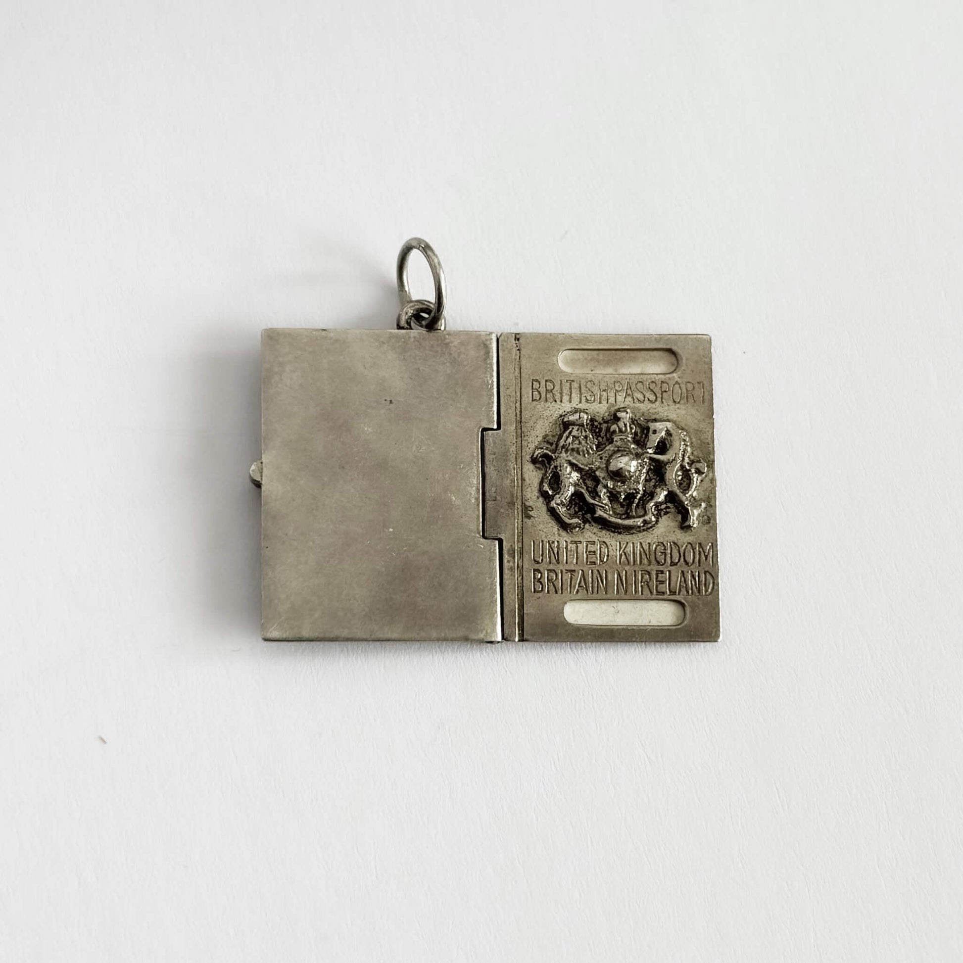 Silver pendant shaped like a British passport on a white background