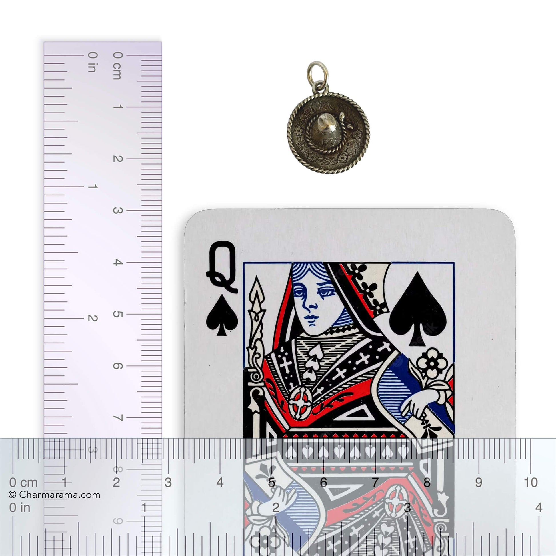 vintage silver sombrero charm with a playing card with a ruler for scale on a white background