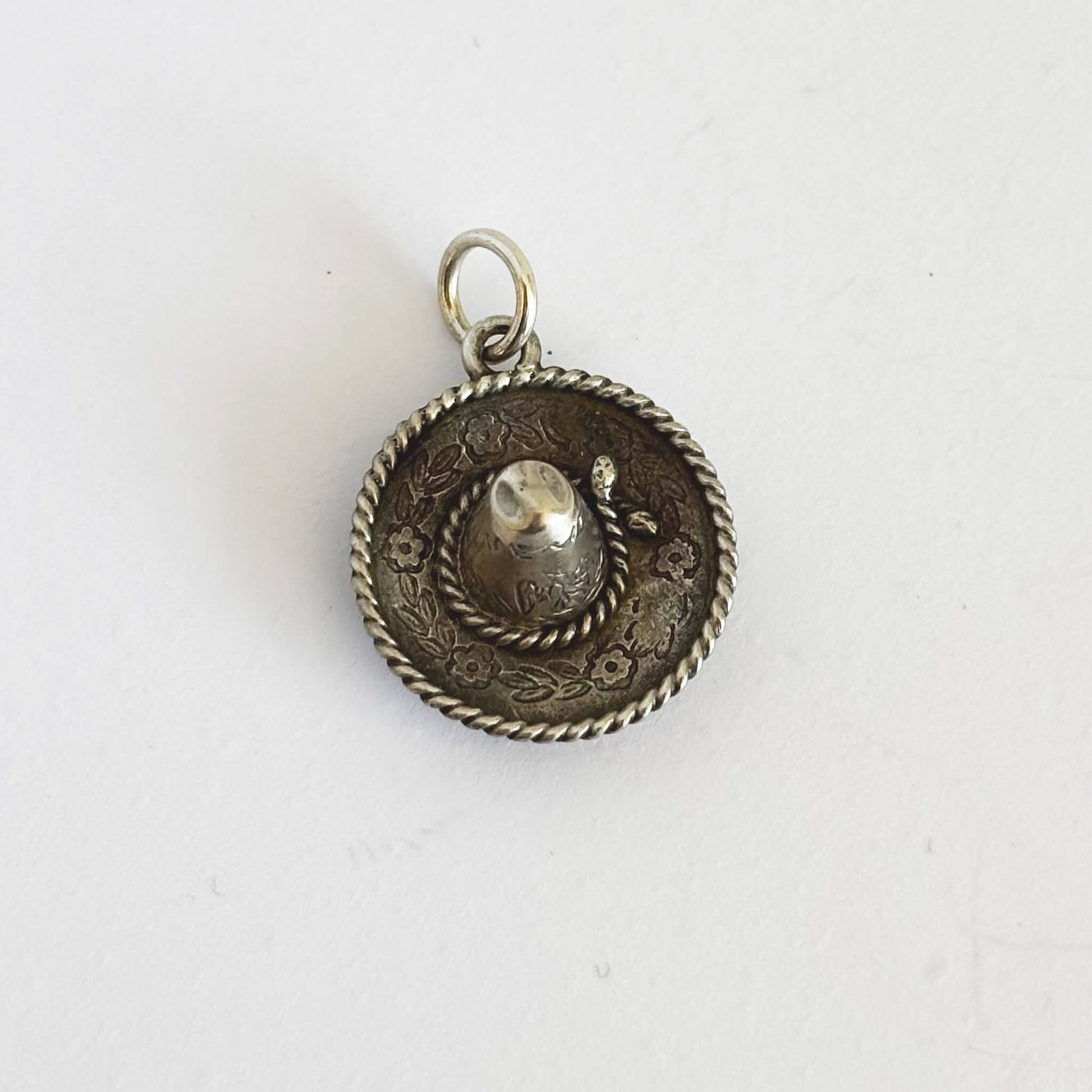 Silver sombrero hat pendant with intricate design on a white background