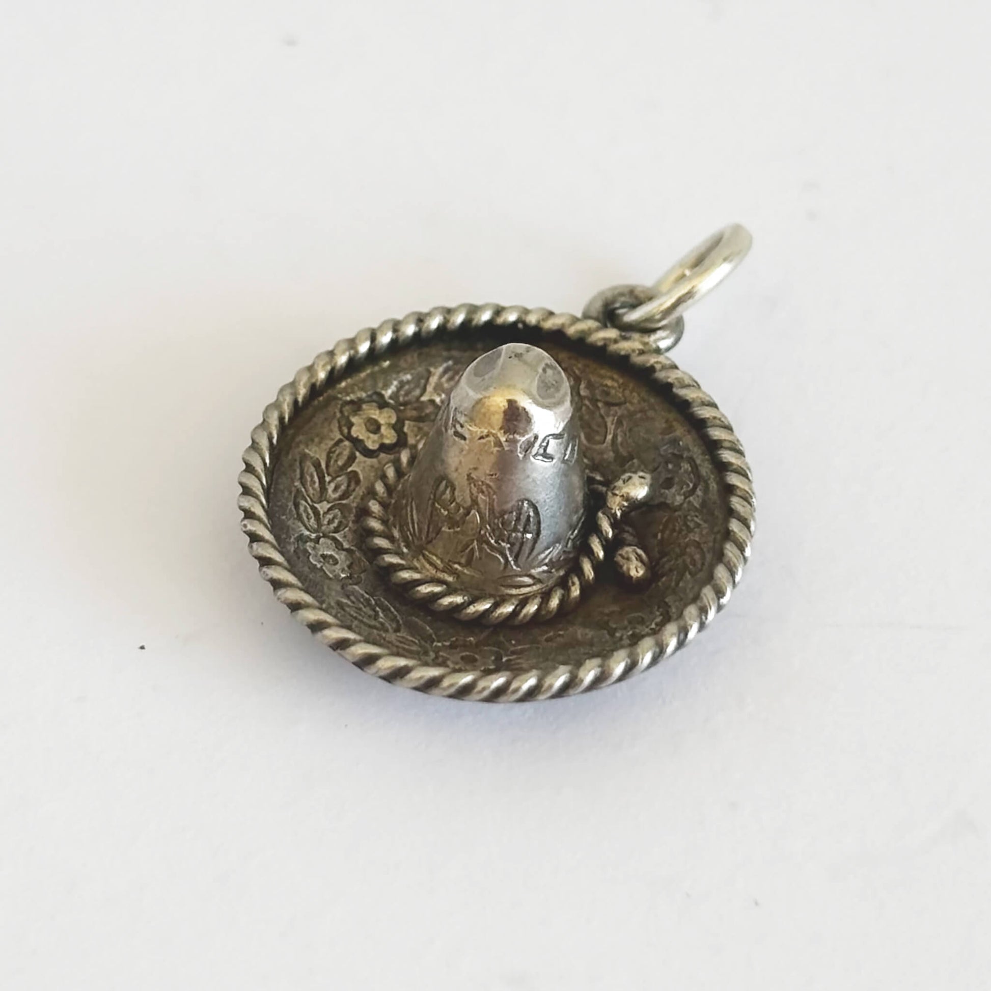 Silver sombrero hat pendant with engraved design on a white background