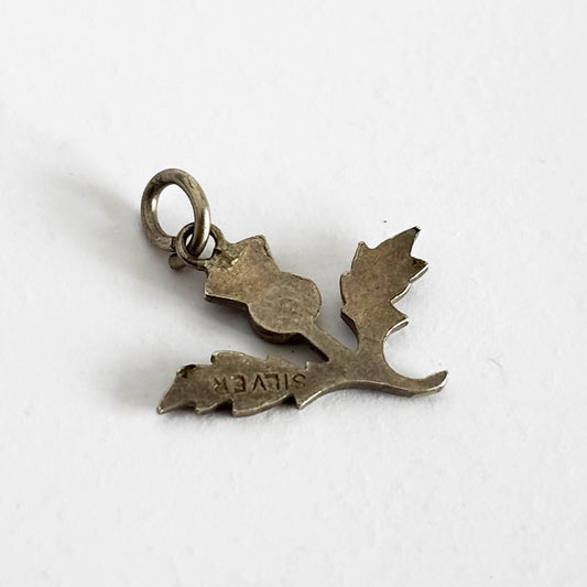 Reverse side of a vintage silver and enamel thistle charm on a white background