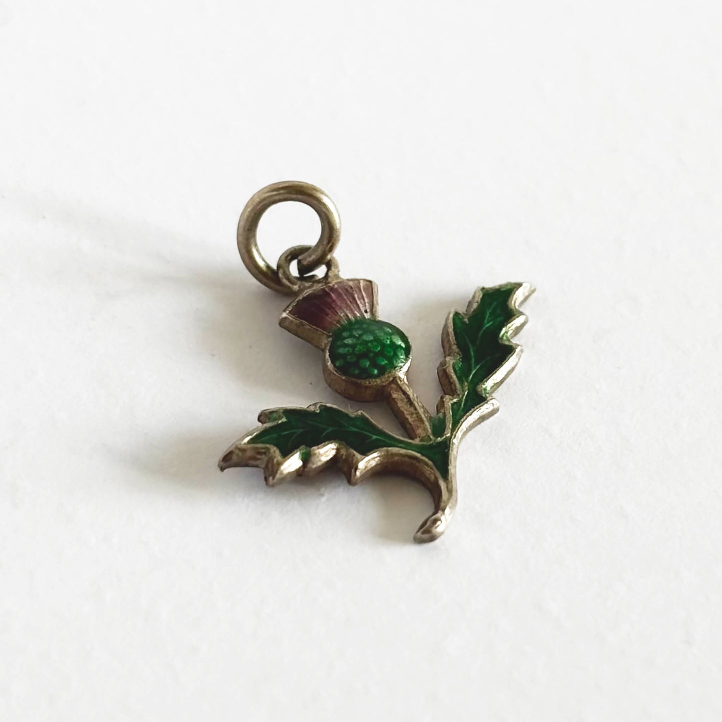 Silver thistle pendant with green enamel on a white background