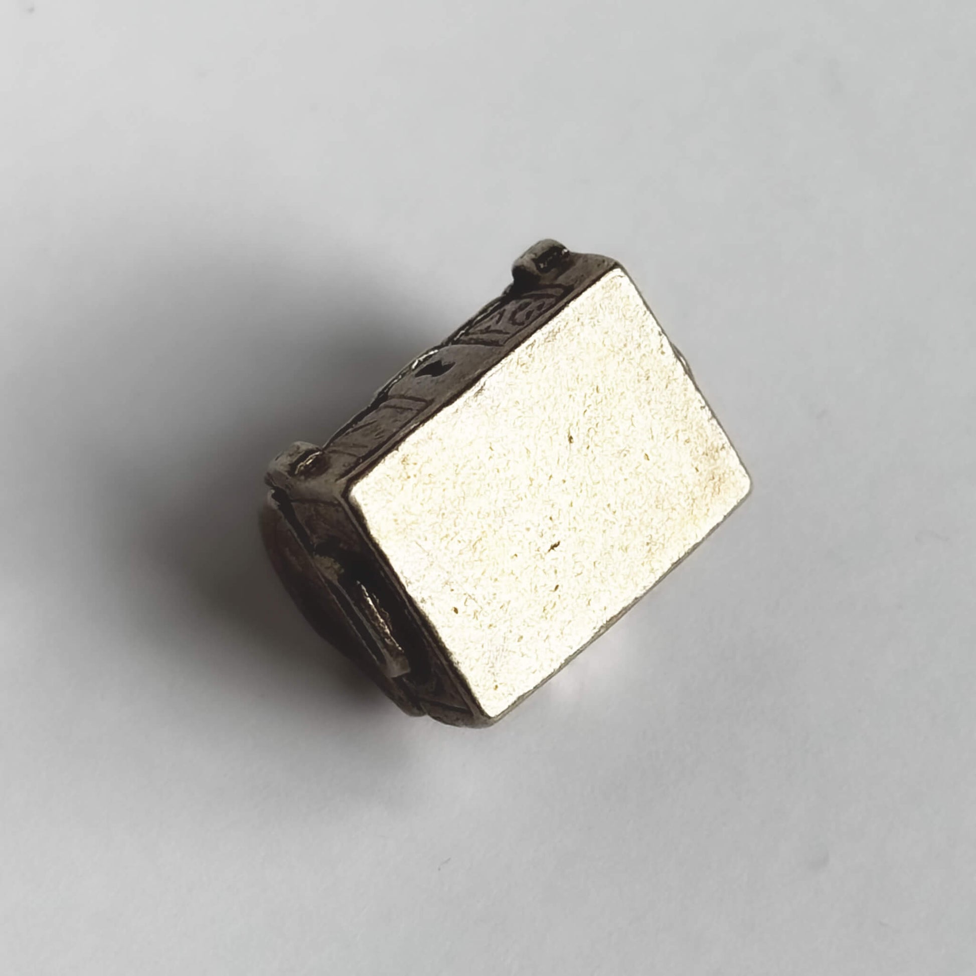Underside of vintage silver treasure chest charm on a white background.