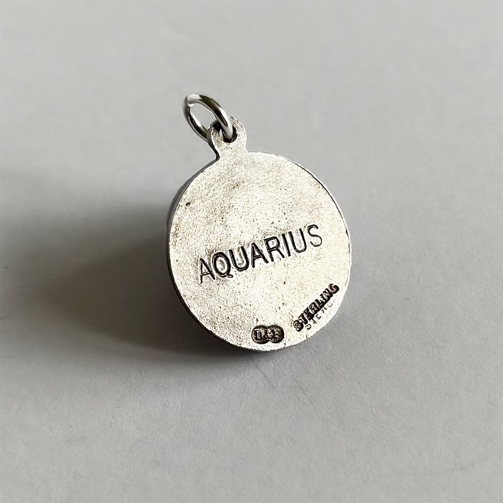 Back of Silver pendant with 'Aquarius' engraved on a grey background