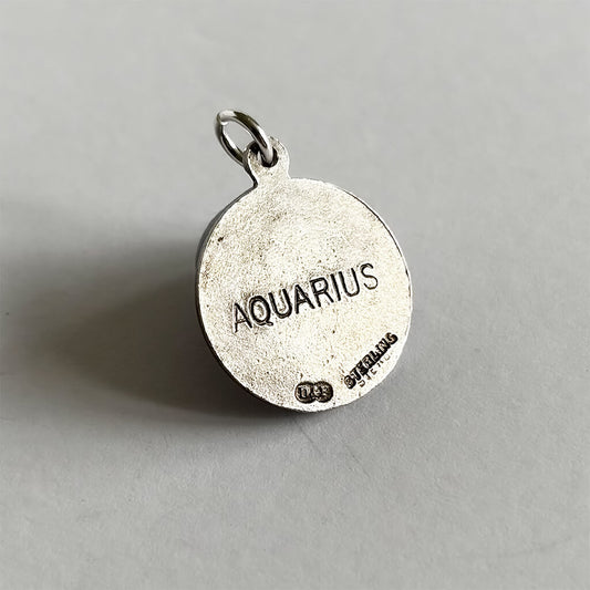 Back of Silver pendant with 'Aquarius' engraved on a grey background