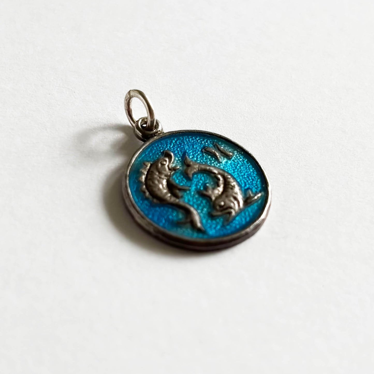 Silver Pisces fish pendant with blue enamel on a white background