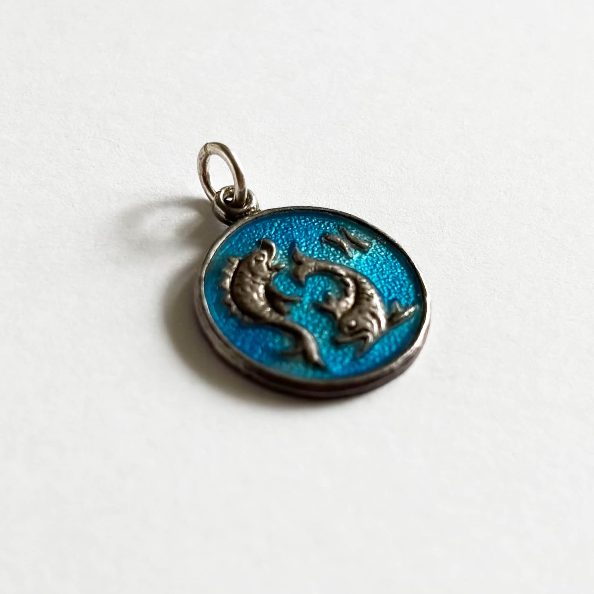 Silver Pisces fish pendant with blue enamel on a white background