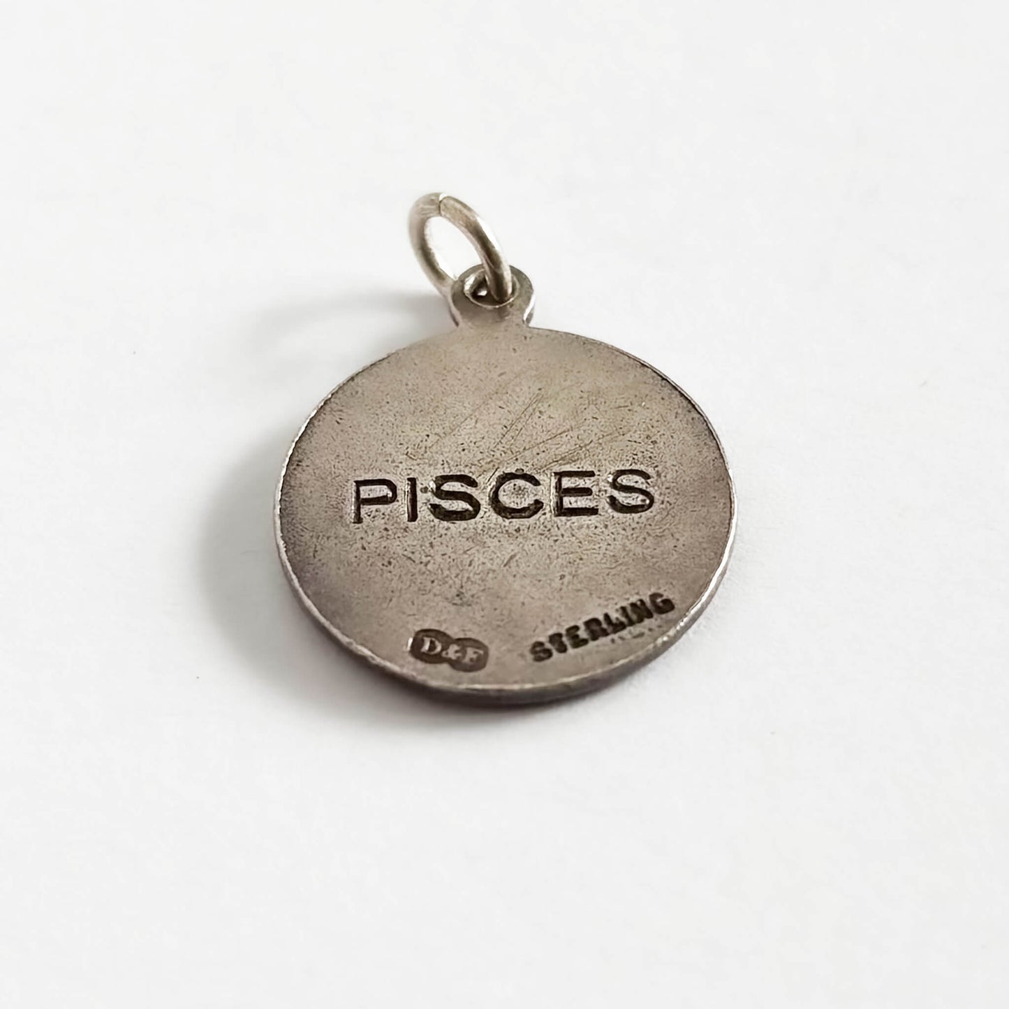 Round sterling silver 'Pisces' zodiac charm on a white background