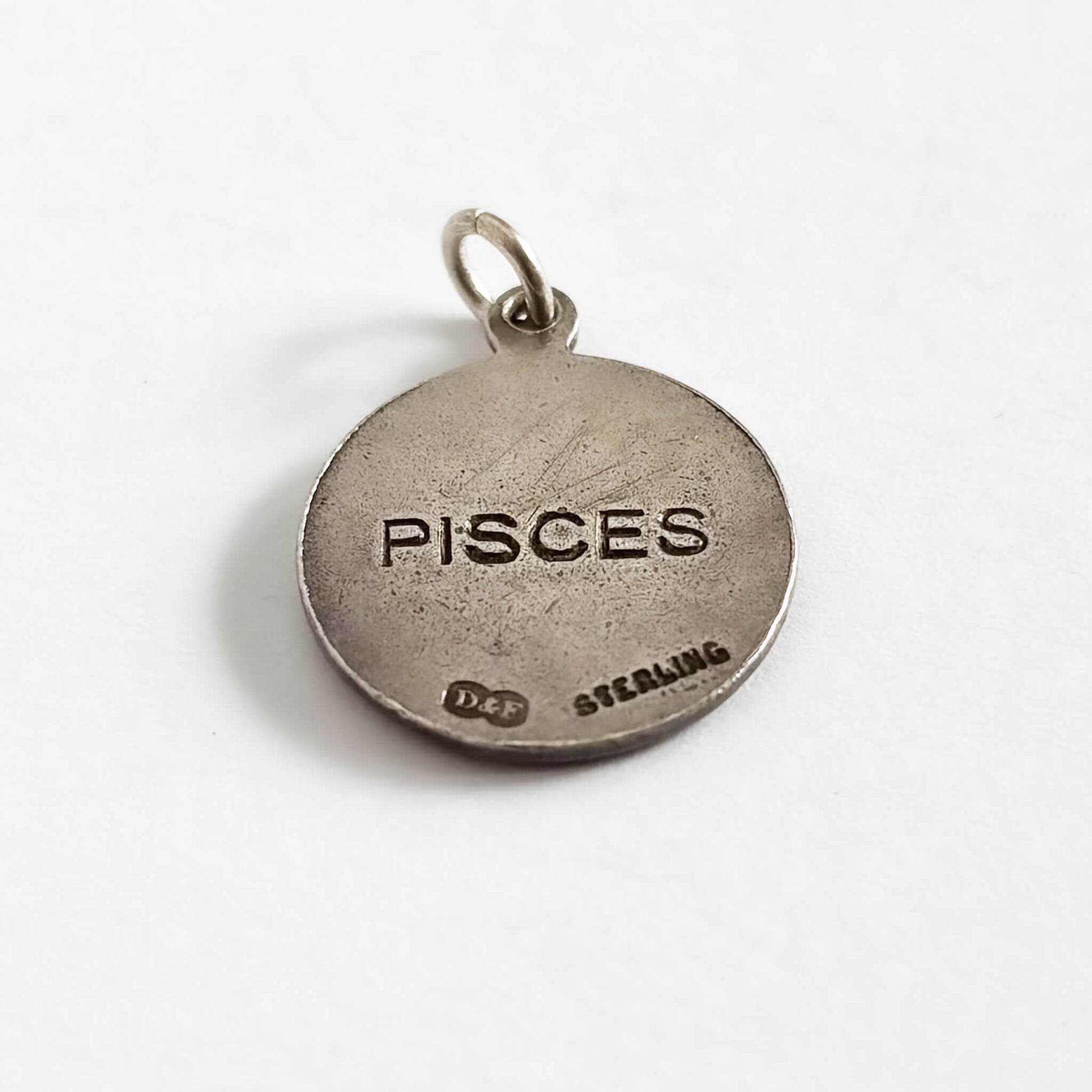 Round sterling silver 'Pisces' zodiac charm on a white background