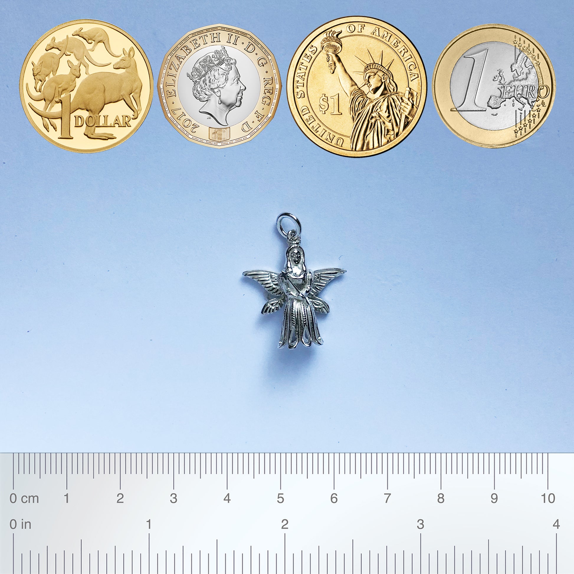 Sterling silver Christmas tree fairy charm with coins and ruler for scale on a grey background