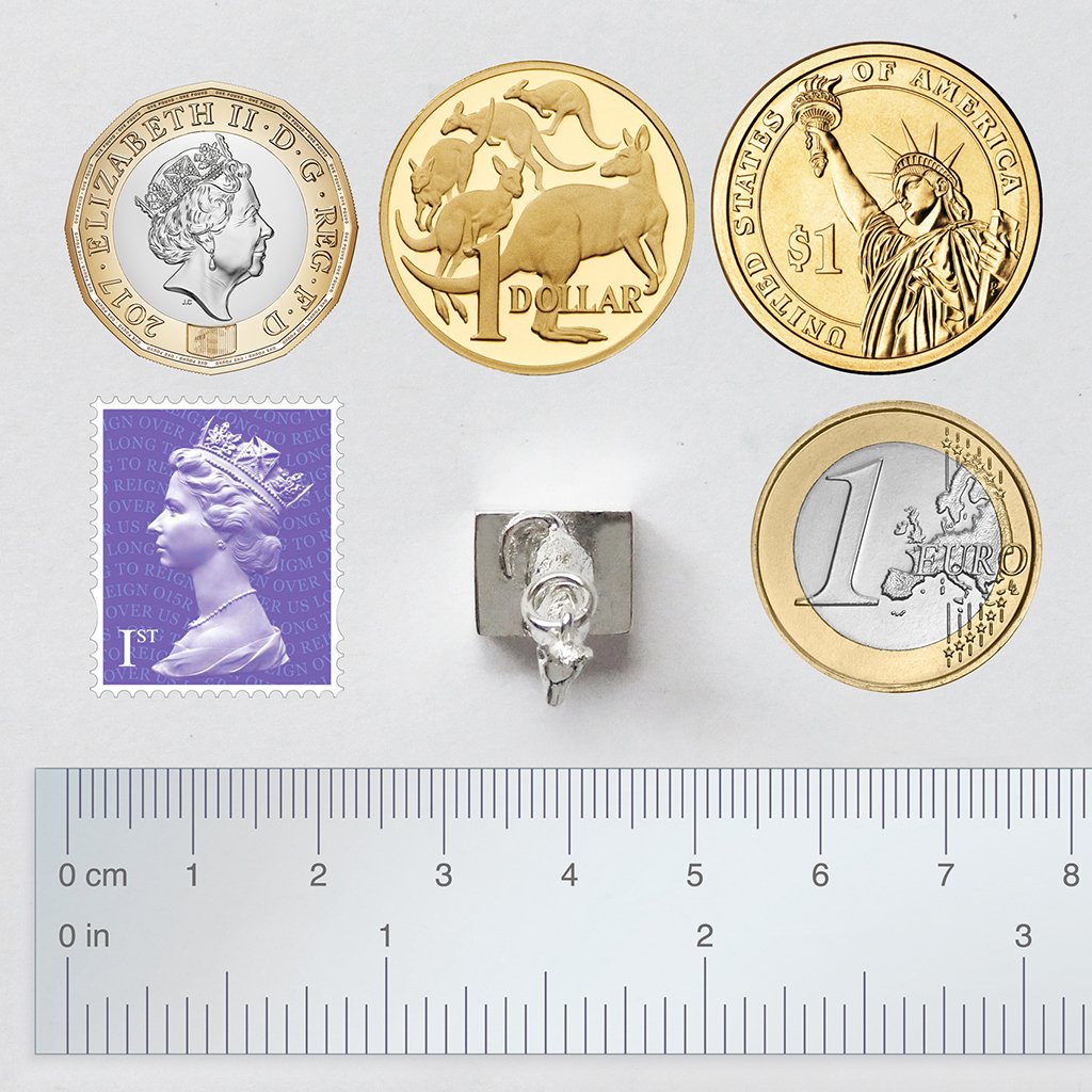 Sterling silver Australian dog on the tucker box charm viewed from above with coins, ruler and postage stamp for scale on a grey background