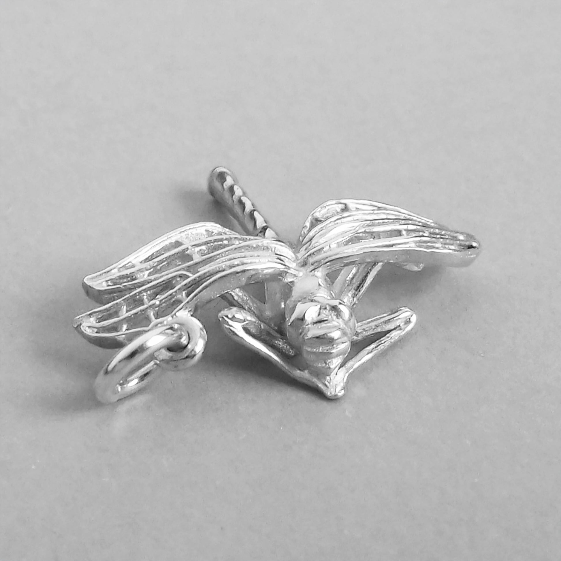 Sterling silver dragonfly charm viewed from front on a grey background