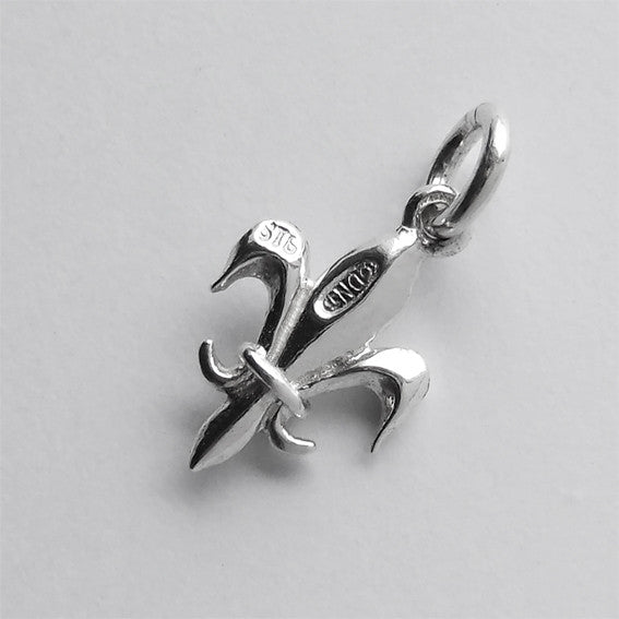 Back of a sterling silver Fleur de lis charm on a grey background