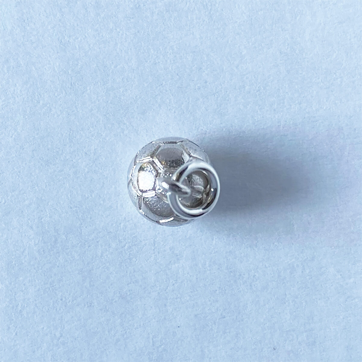 Sterling silver football charm viewed from above on a grey background
