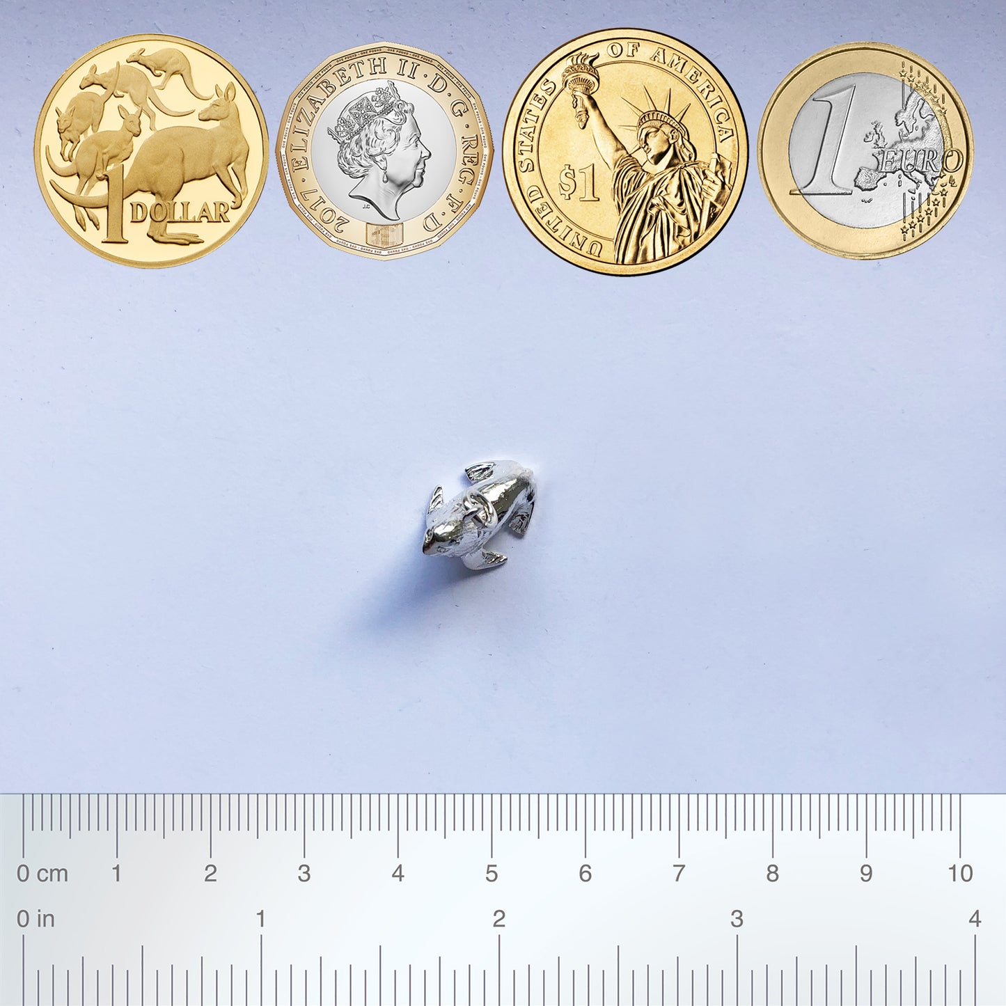 Sterling silver fur seal charm with coins and ruler for scale on a grey background