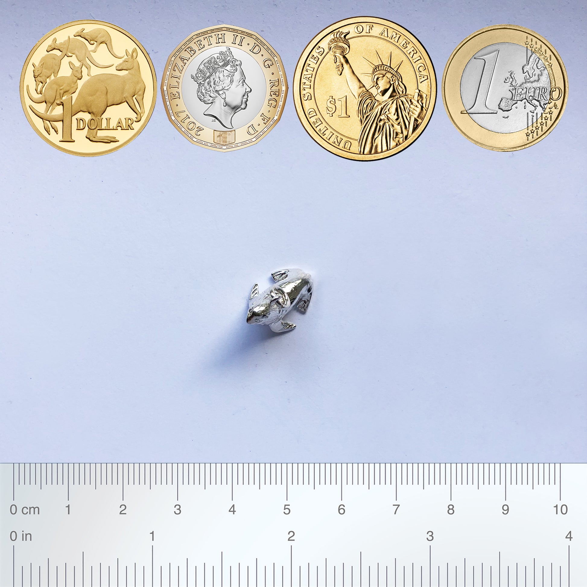 Sterling silver fur seal charm with coins and ruler for scale on a grey background