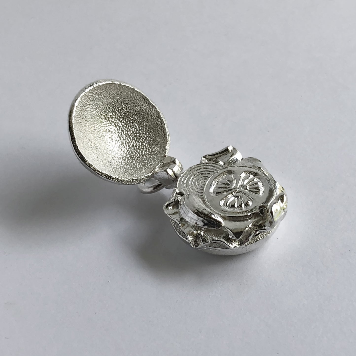 Sterling silver hamburger charm open to tomato and onion slices  on a grey background
