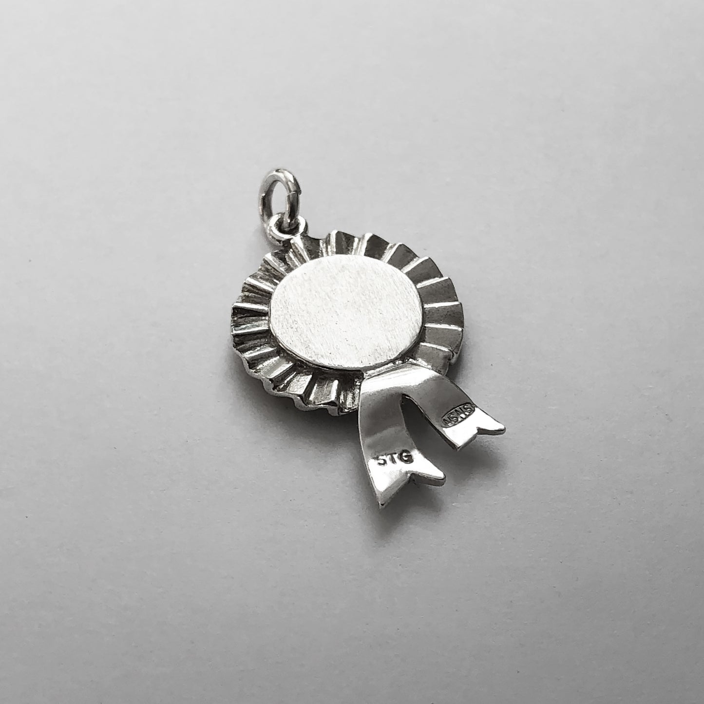 Back of a sterling silver first prize rosette charm on a grey background