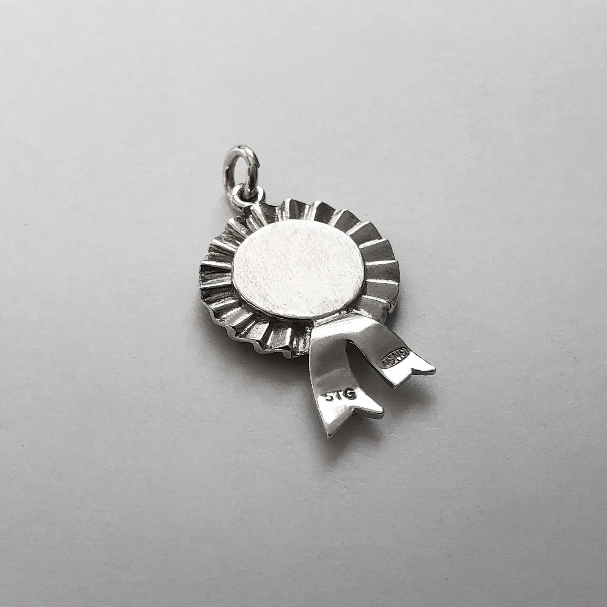 Back of a sterling silver first prize rosette charm on a grey background