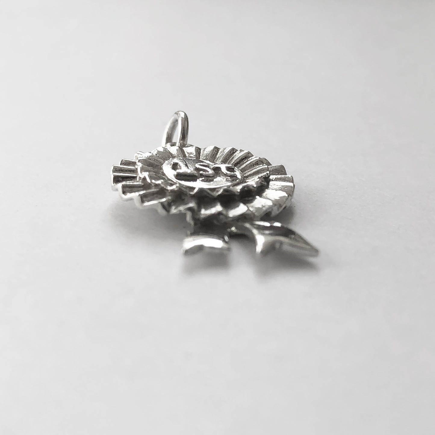 Side view of sterling silver first prize rosette charm on a white background