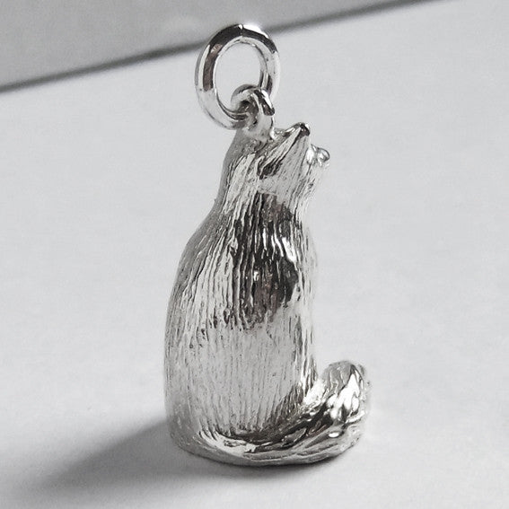 A sitting silver Birman cat charm on a grey background.