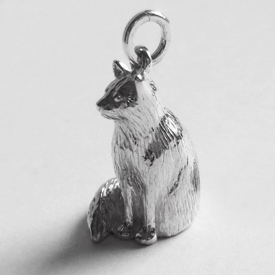 A sitting silver Birman cat charm on a grey background.