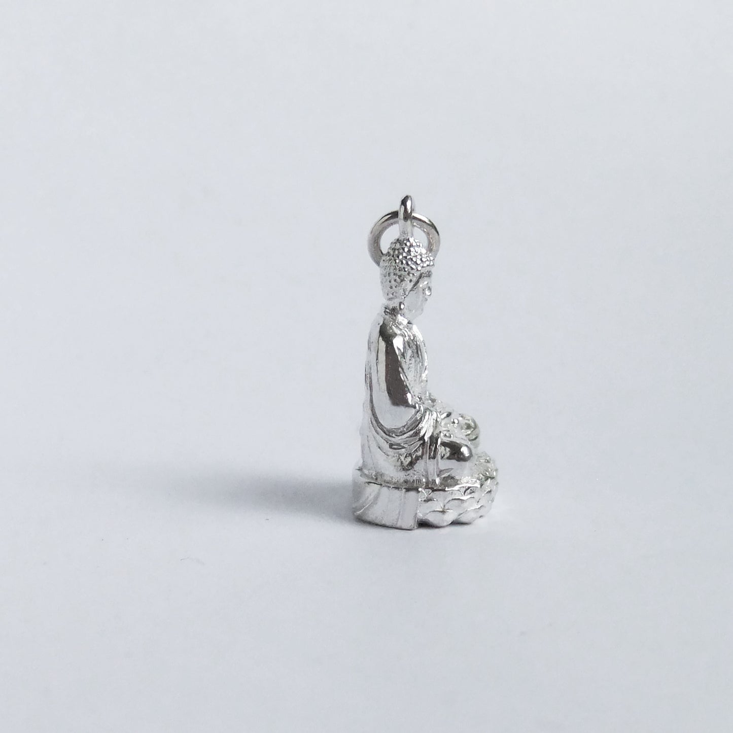 Silver buddha charm pictured from side on light grey background