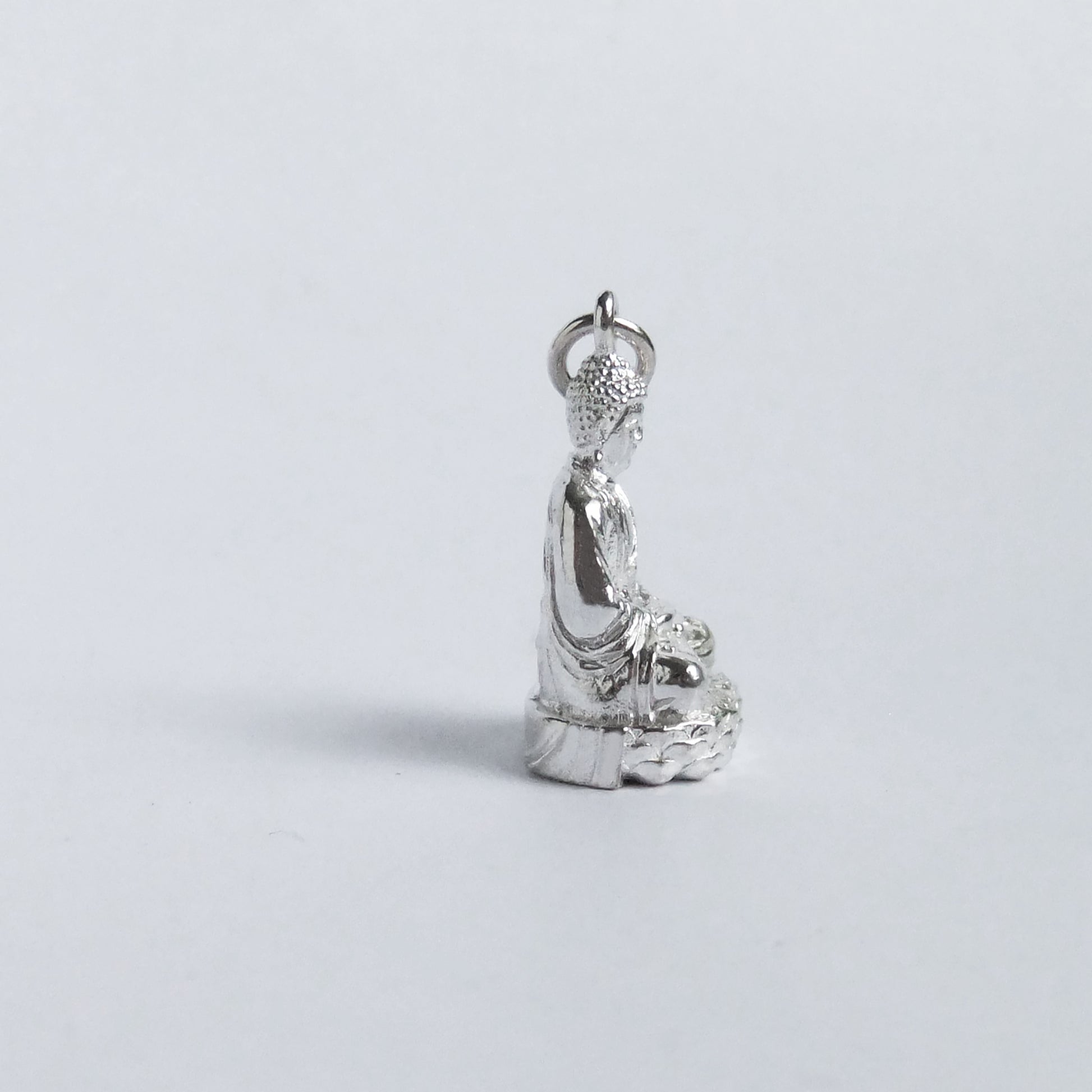 Silver buddha charm pictured from side on light grey background