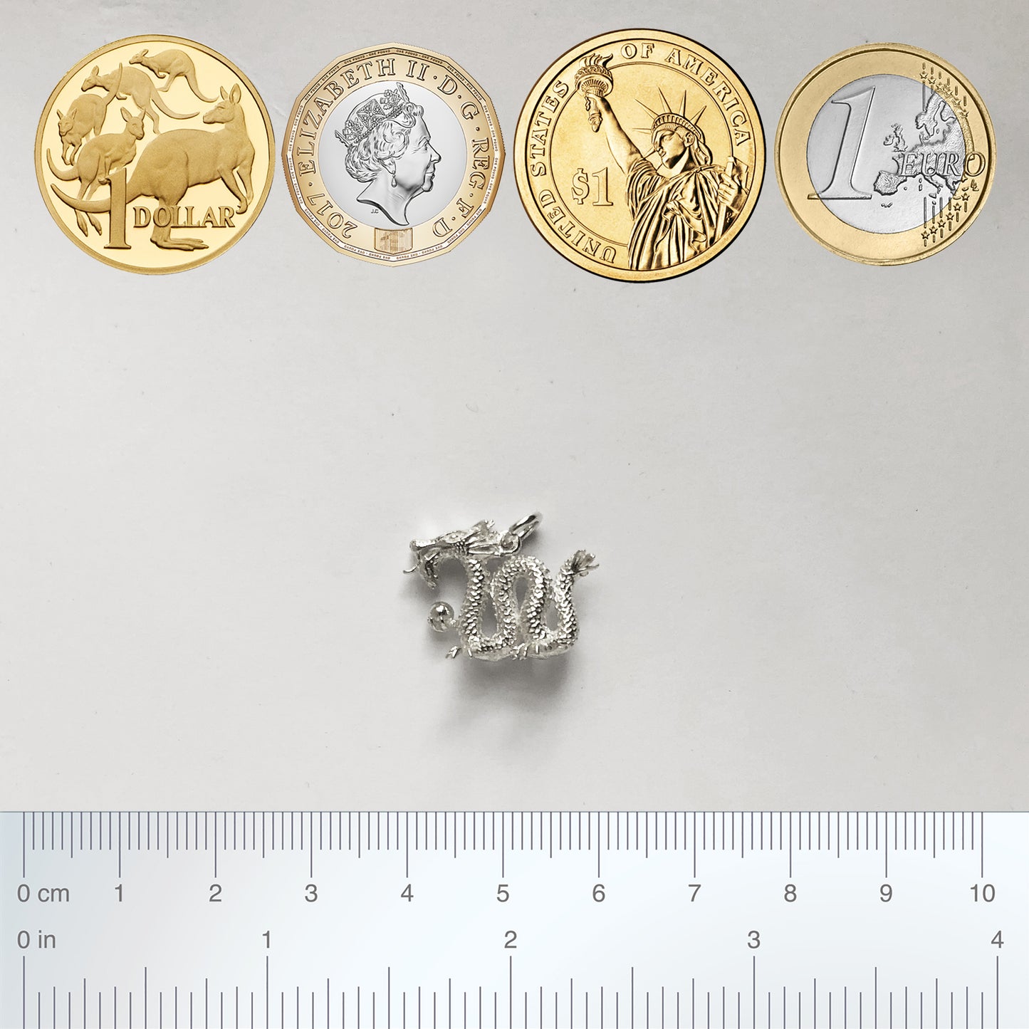 silver Chinese dragon charm with coins and ruler for scale
