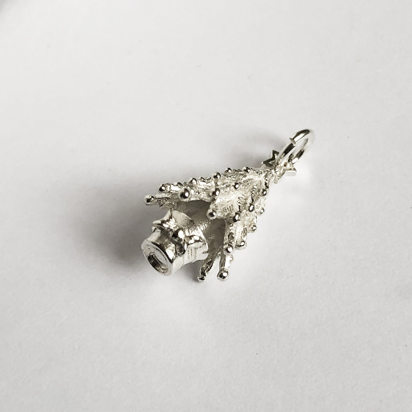 silver Christmas tree charm seen from side on a light grey background