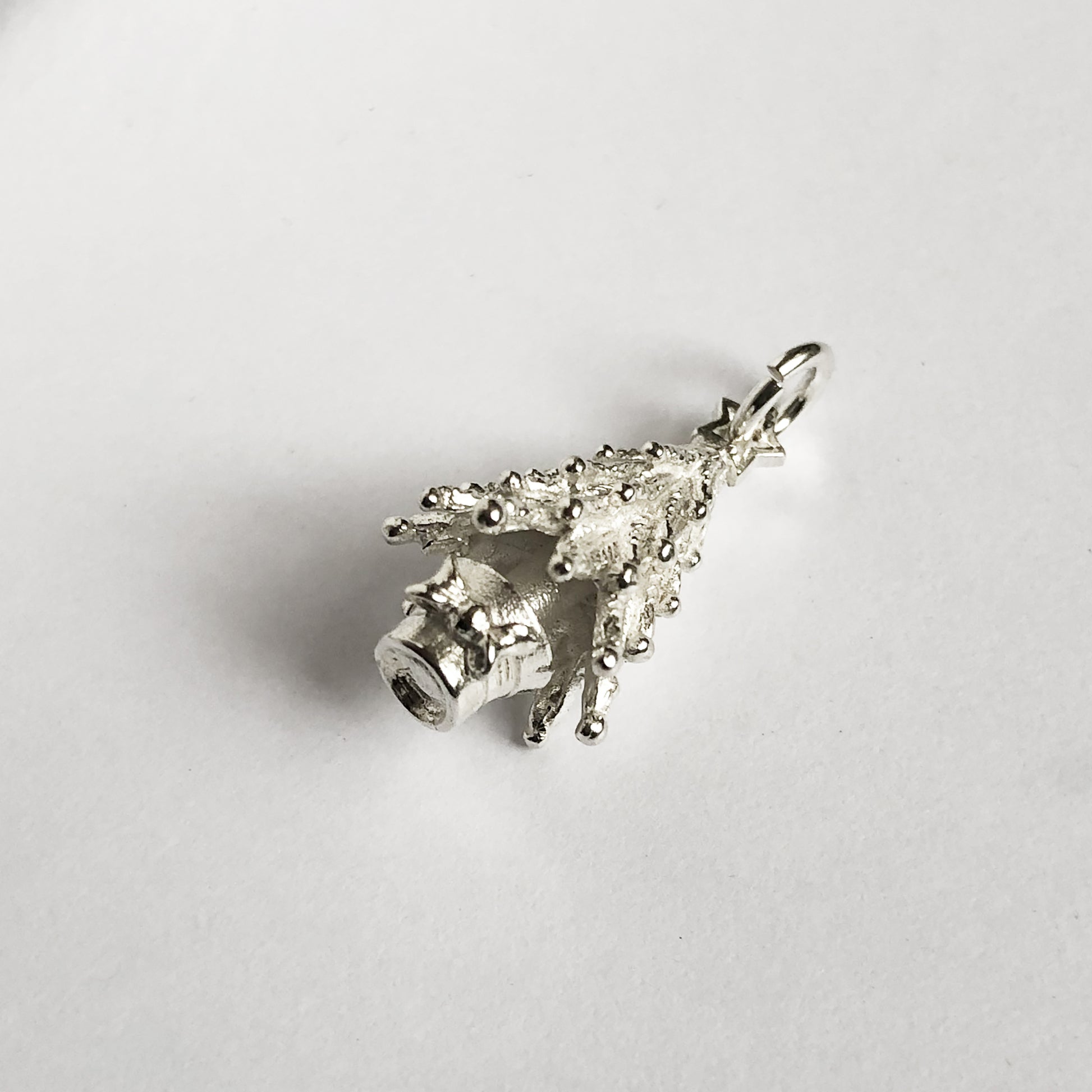 silver Christmas tree charm seen from side on a light grey background