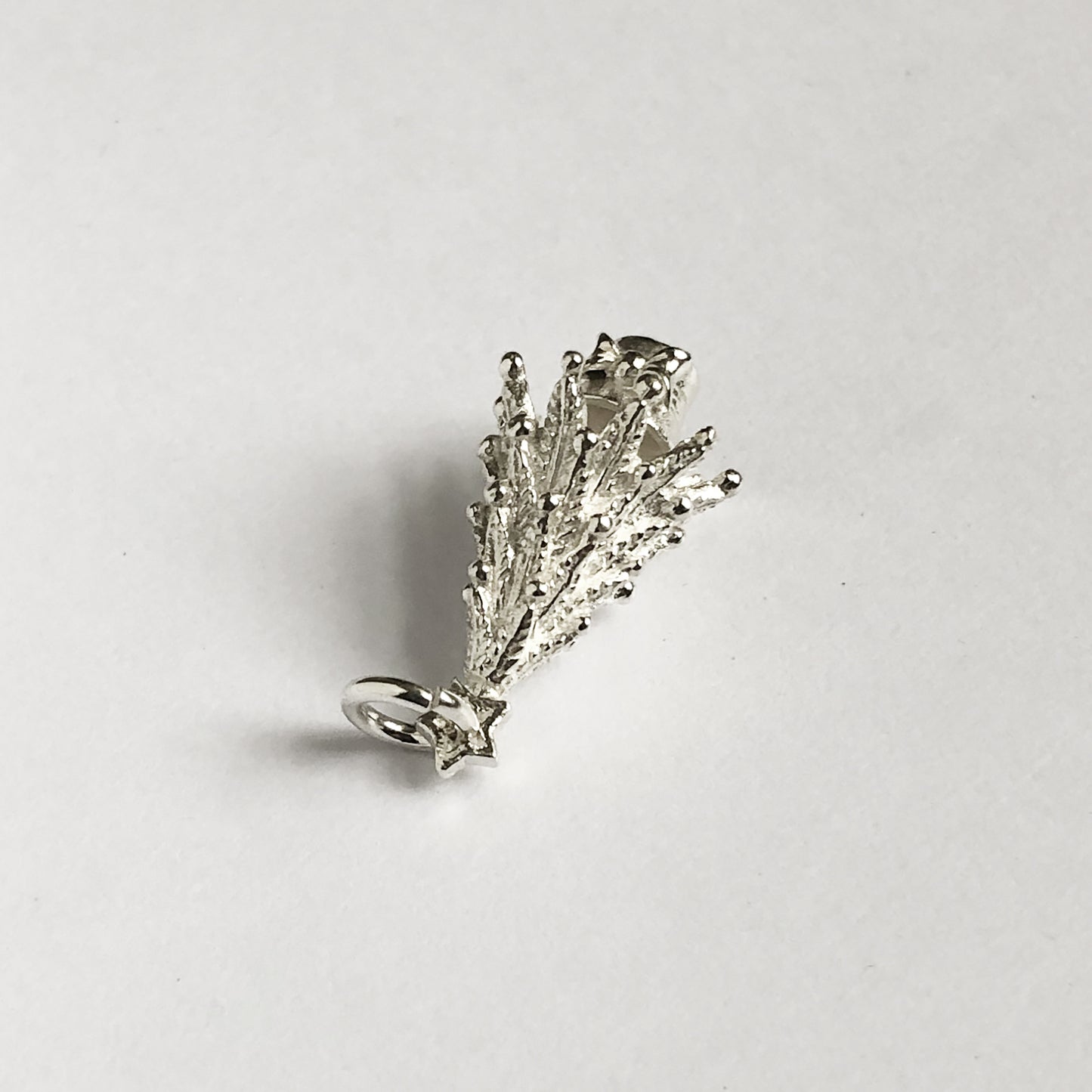 silver Christmas tree charm seen from side on a light grey background