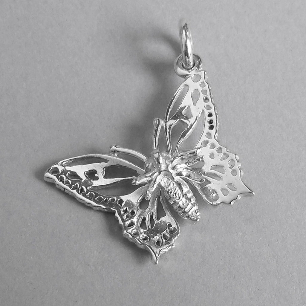 A silver filigree butterfly charm underside on a grey background.