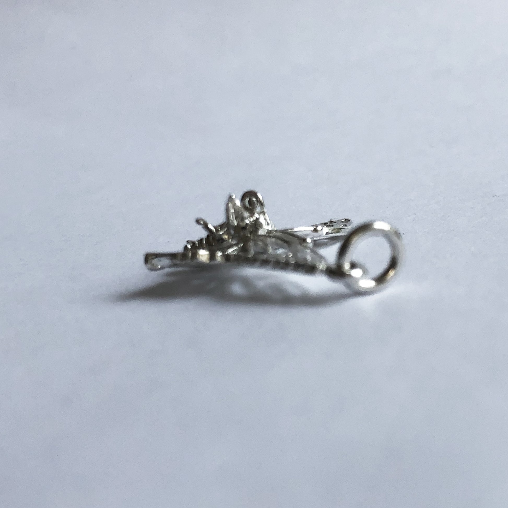 A silver filigree butterfly charm underside side view on a grey background.