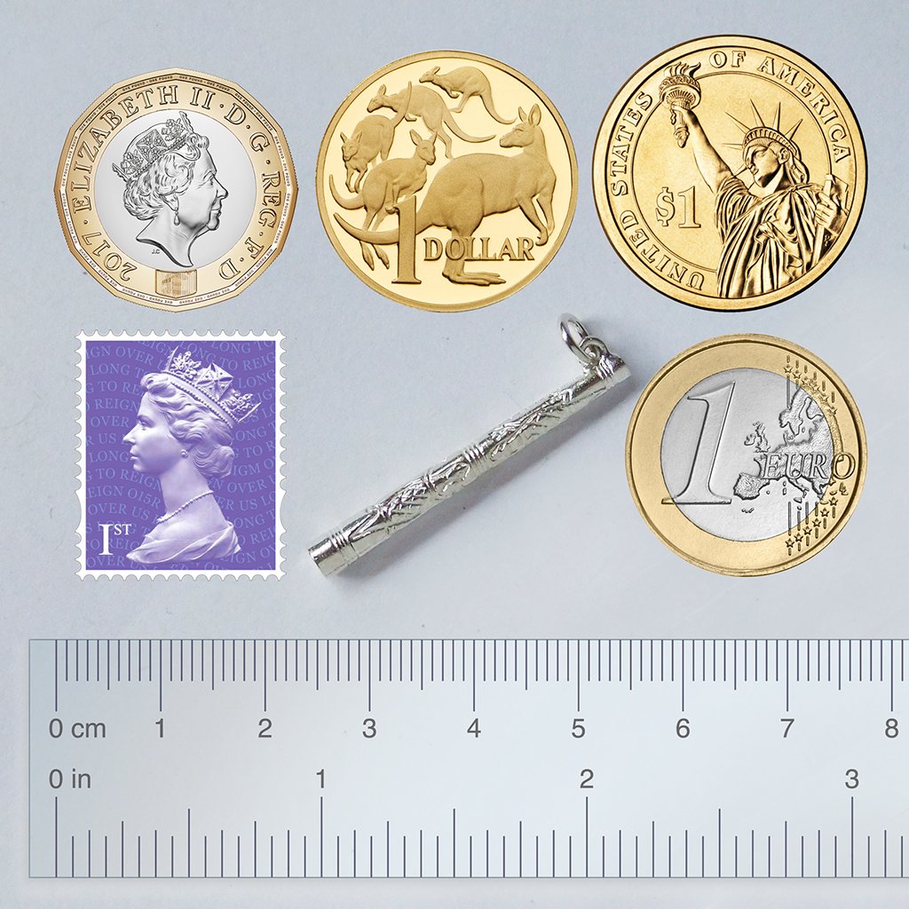 Sterling silver Didgeridoo charm with coins postage stamp and ruler for scale on a light grey background