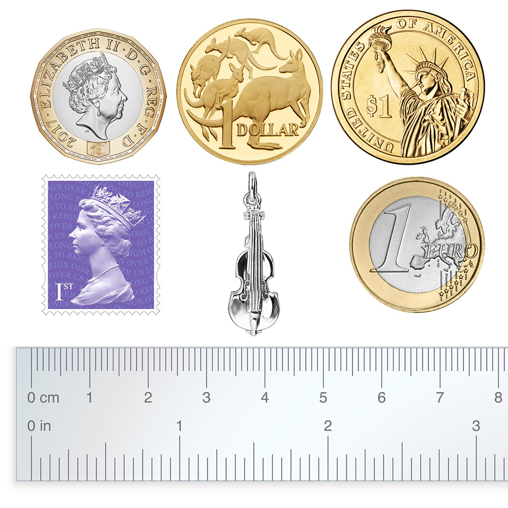 silver violin charm with coins, stamp and ruler for scale on a white background