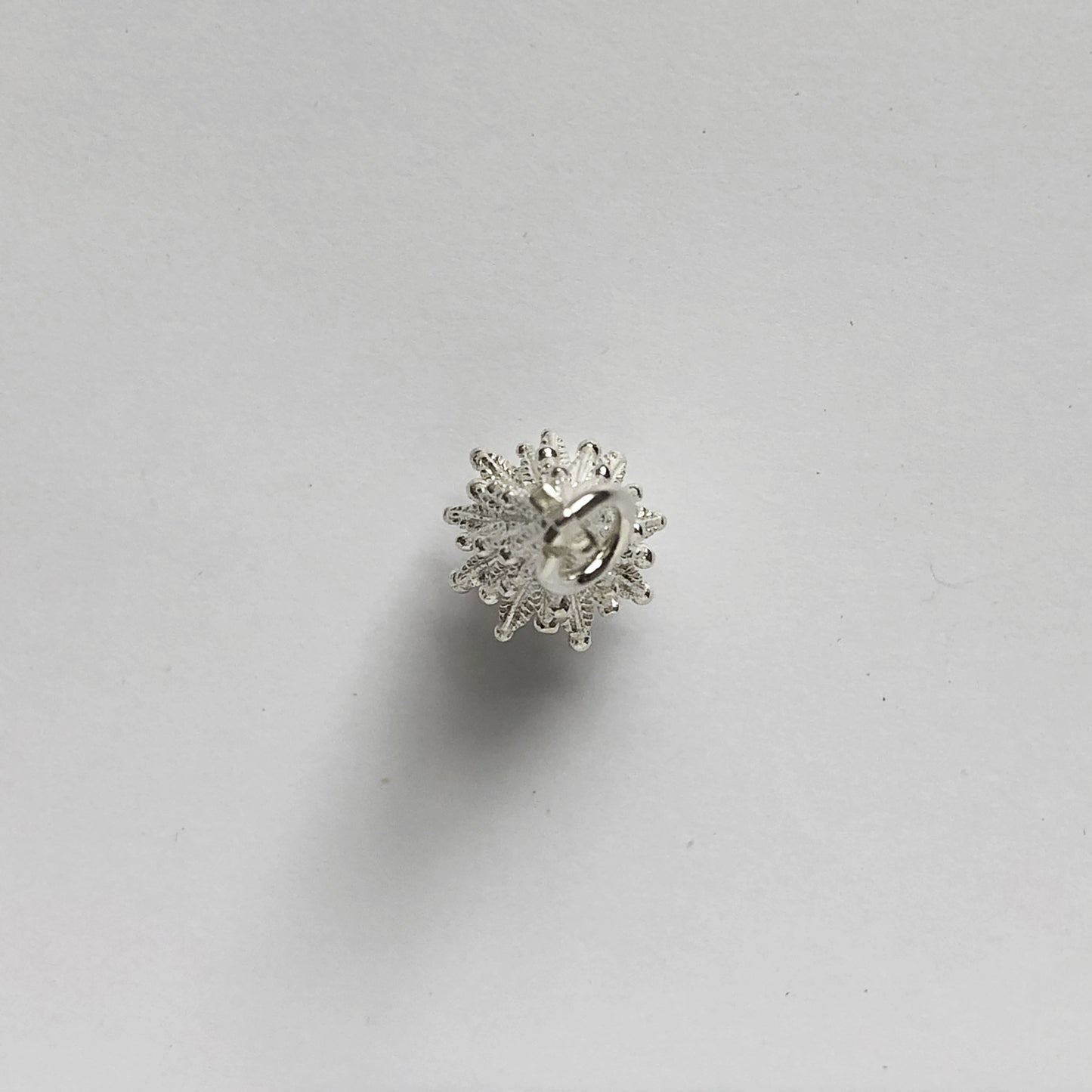 silver Christmas tree charm seen from above on a light grey background
