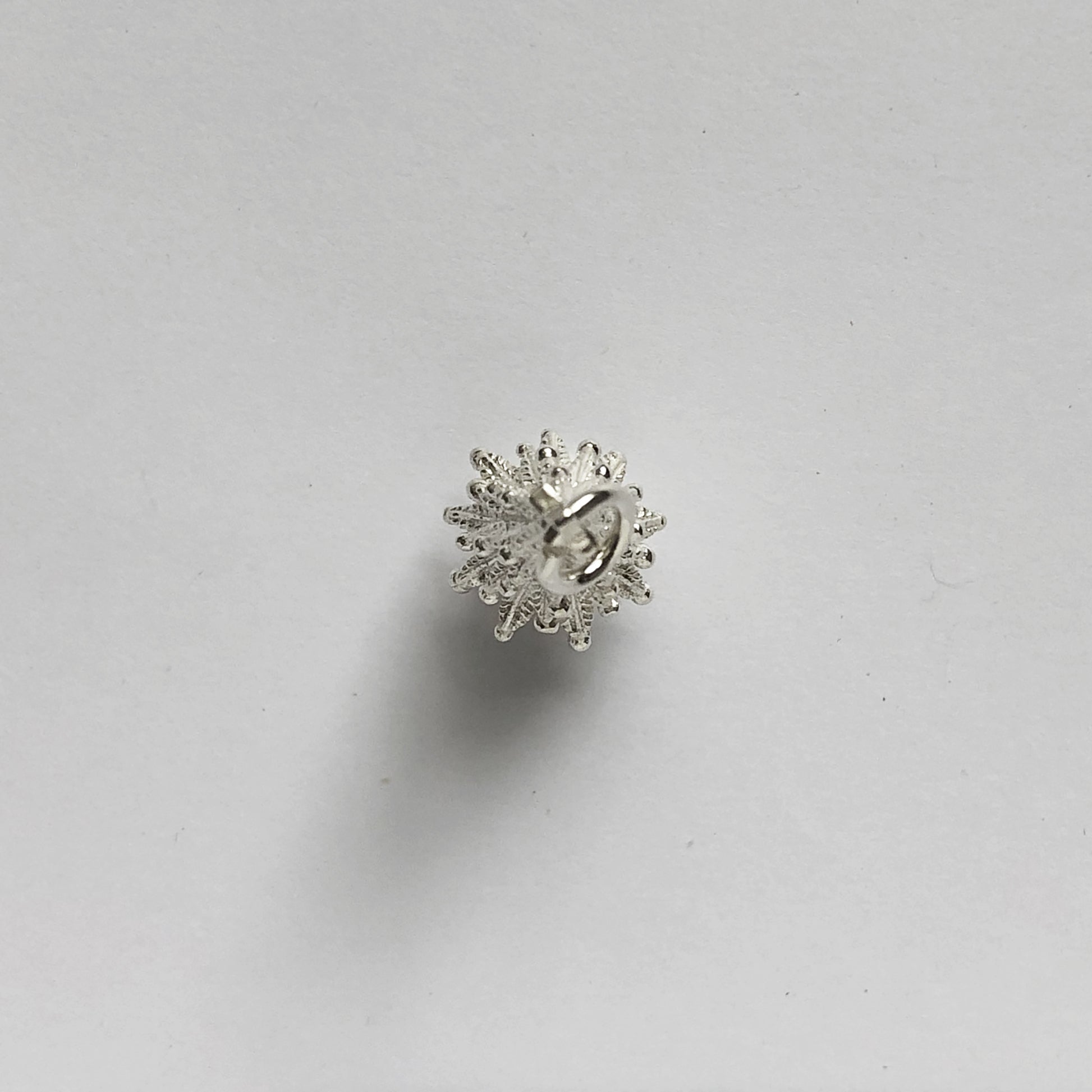 silver Christmas tree charm seen from above on a light grey background