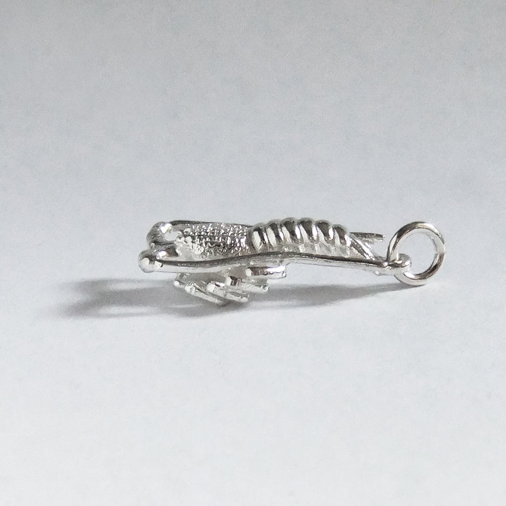silver crayfish charm seen from side on light grey background