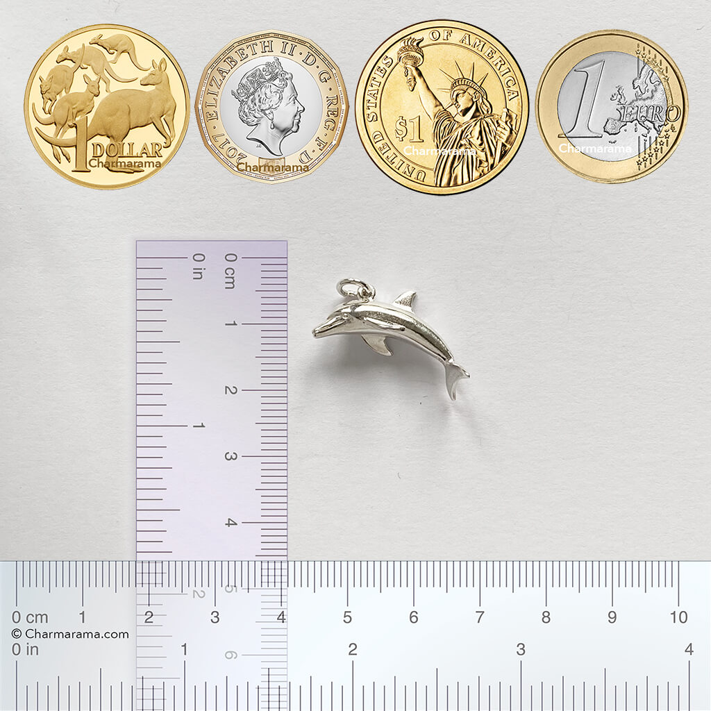 Sterling silver dolphin charm with coins and ruler for scale on a grey background